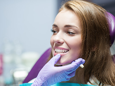 A woman sitting in a dental chair, smiling at the camera while wearing a face mask.