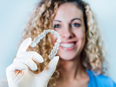 A woman, likely a dental professional, holds up a transparent retainer with a smile.
