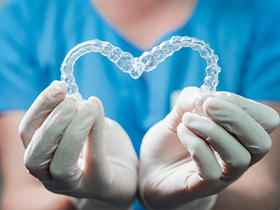 A dental hygienist s hands holding a clear plastic heart with transparent braces inside.