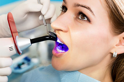 A woman receiving a dental cleaning with a device that sprays water, under the supervision of a dentist in a professional setting.