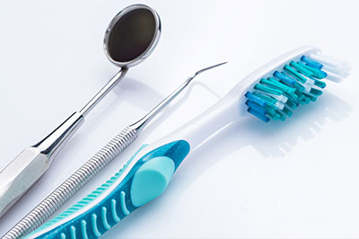 A collection of dental hygiene tools, including a toothbrush with blue bristles and a metal dental pick, displayed on a white background.