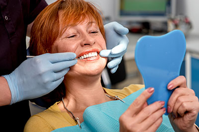 Woman in dental chair, smiling and holding blue mouthguard, while dental professional works on her teeth.