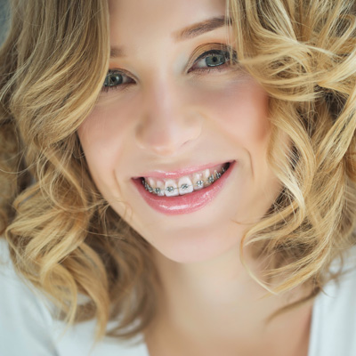 A woman with a wide smile, showing her braces and teeth, posing for a portrait.