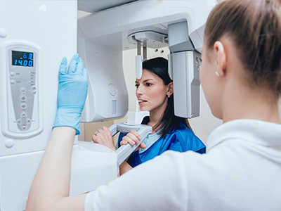 Two individuals in a medical or dental setting, one operating a large piece of equipment while the other observes.