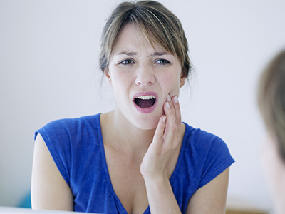 The image shows a woman with her mouth open, possibly expressing surprise or concern, looking at her own reflection in the mirror.