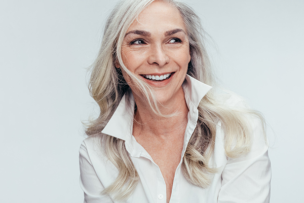 The image features a woman with short hair, wearing a white top and smiling at the camera.