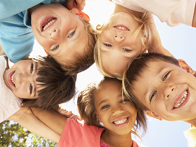 A group of children in a joyful circle, smiling and posing for the camera under a clear sky.