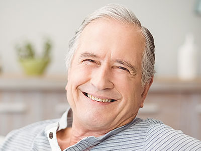 The image shows an elderly man with a smile, sitting in a chair.