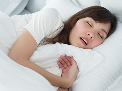 A woman is lying in bed, appearing to be asleep with her eyes closed.