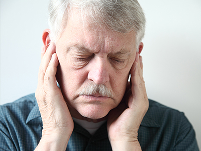 An elderly man with a mustache, holding his hand to his ear, appearing to be in pain or discomfort.