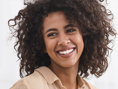 A smiling woman with curly hair and a bright smile, wearing a light-colored top.